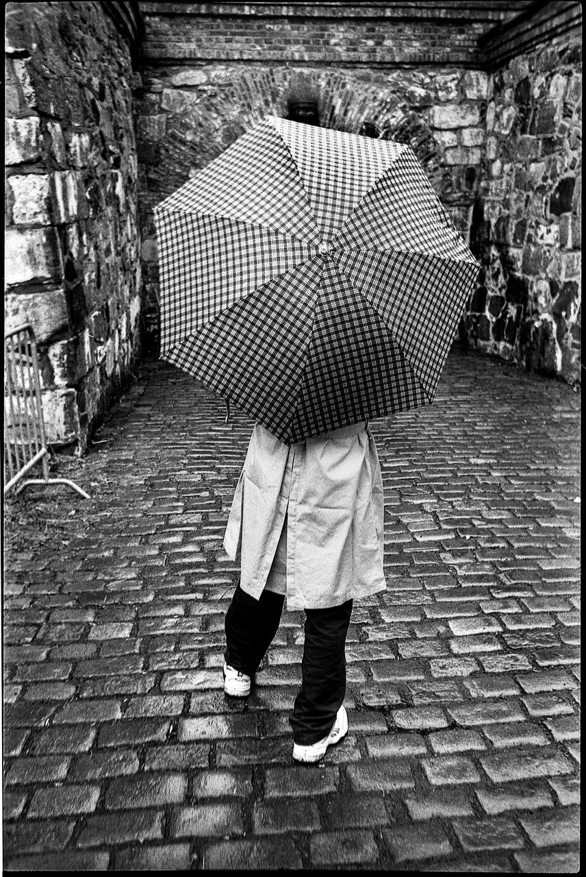 real people, one person, architecture, full length, brick, wall, women, brick wall, walking, umbrella, day, low section, rear view, lifestyles, standing, leisure activity, protection, built structure, stone wall, outdoors, rainy season, rain, paving stone, obscured face