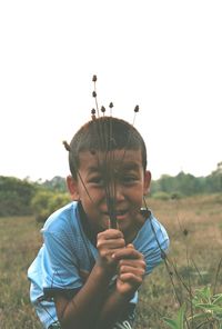 Boy holding dry plants while bending on land against clear sky