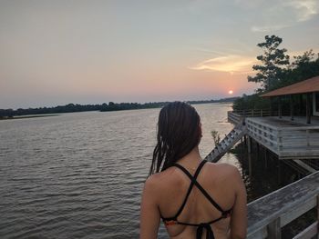 Rear view of woman standing by sea against sky during sunset