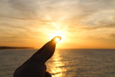 Close-up of hand holding utility knife against sea during sunset