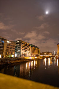 Illuminated buildings by river against sky at night