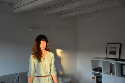 Sunlight falling on woman standing against wall at home