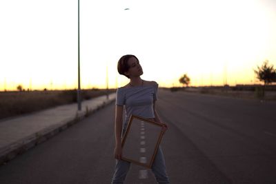 Young woman holding mirror with reflection on road during sunset