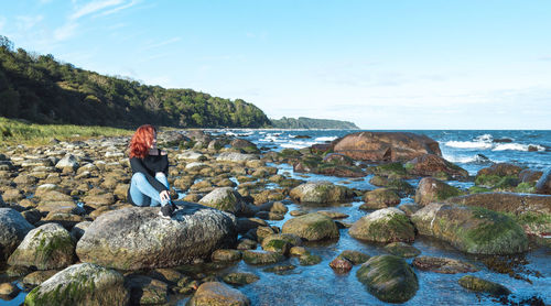 Man standing on rock by sea against sky