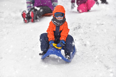 Full length of boy tobogganing on snowy field