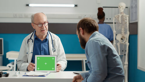 Senior doctor showing digital tablet screen to patient at clinic