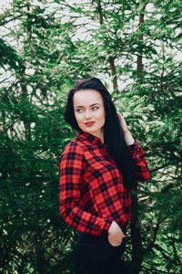 Smiling young woman looking away while standing against trees in forest