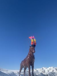 Horse standing on snow covered field against clear blue sky