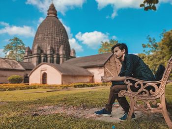 Man looking away while sitting on bench in temple against sky