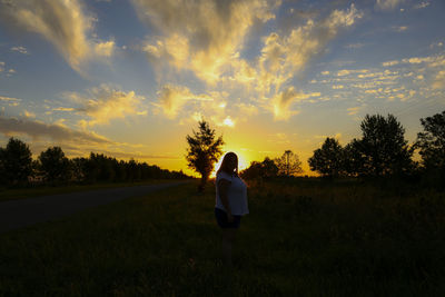 Rear view of woman standing on field against sky during sunset