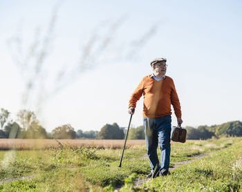 Senior man carrying traveling bag, walking in the fields