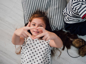 Portrait of smiling girl making heart shape while lying on floor at home