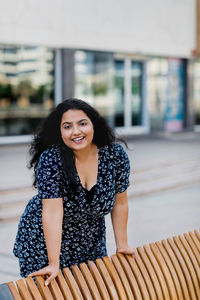 A charming indian woman stands by the bench and smiles.