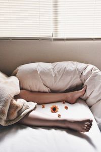 Low section of woman relaxing on bed with flowers at home