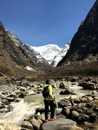 Rear view of woman hiking while standing on rocks against clear blue sky during sunny day