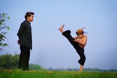 Male instructor watching at boy practicing kung fu on field against sky