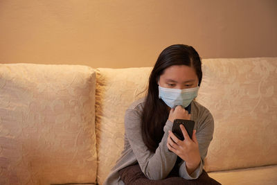 Girl wearing mask using smart phone sitting at home