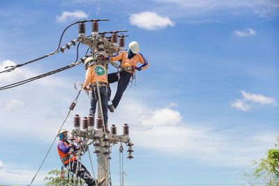 Low angle view of men hanging on telephone pole against sky