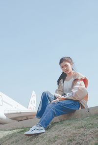 Side view of smiling young woman sitting on land against clear sky