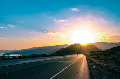 Road by mountains against sky during sunset