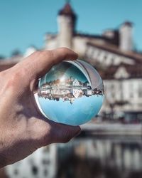 Cropped hand holding crystal ball with reflection of city