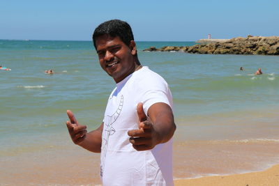 Portrait of mid adult man gesturing while standing at beach against sky