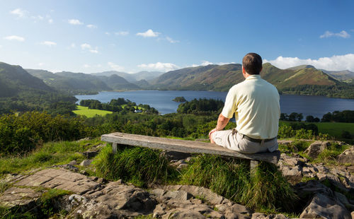 Rear view of man sitting on mountain against sky