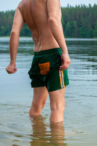 Midsection of shirtless man standing in lake