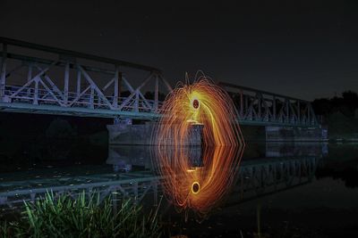 Illuminated bridge over river against sky at night