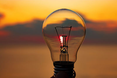 Close-up of light bulb against sky during sunset