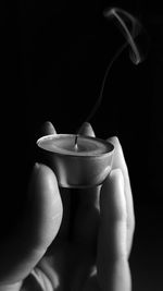 Cropped image of hand holding tea light against black background