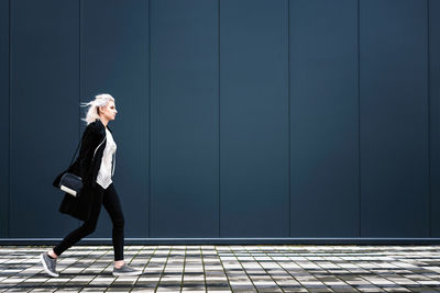 Side view of young woman walking on footpath against wall