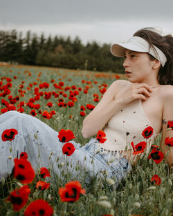 Portrait of young woman standing by flowering plants on field