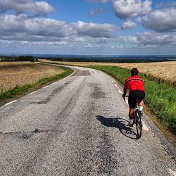 Rear view of man riding bicycle on road against sky