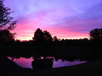 Silhouette trees by lake against romantic sky at sunset