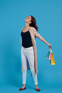 Woman holding shopping bags while standing against blue background