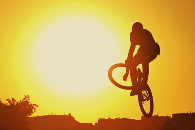 Silhouette person jumping while riding bicycle against sky during sunset