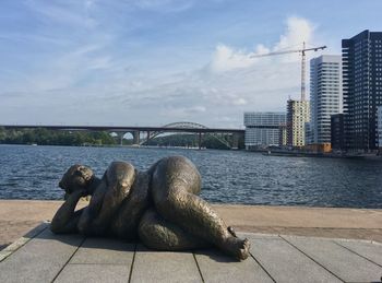 Sculpture on bridge over river in city against sky