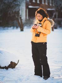 Woman using mobile phone while standing on snow covered field