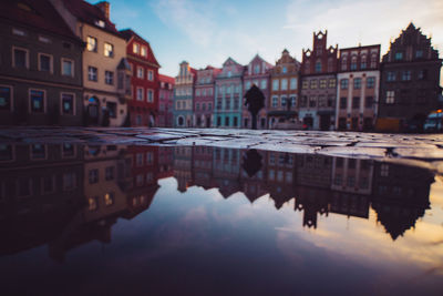 Surface level shot of buildings with puddle in foreground during sunset