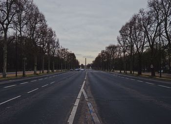 Road by trees in city against sky