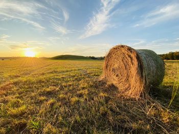 Hay bales on field against sky during sunset