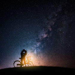 Silhouette couple romancing by bicycle against star field at night