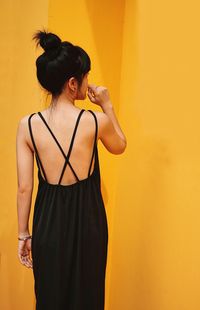 Rear view of woman standing against yellow wall