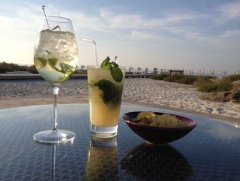 Close-up of drinks with chips on table at beach against sky