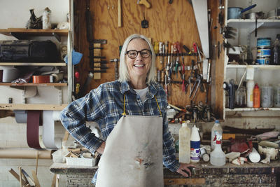 Portrait of smiling senior owner standing against tools at workshop