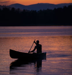 Silhouette man on boat in lake against sky during sunset