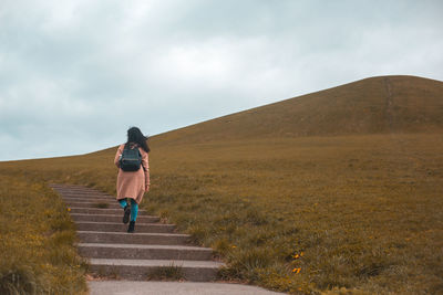Rear view of woman walking on steps against sky