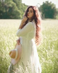 Woman with long hair curls in the green meadow wearing white dress in summer. 