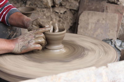 Midsection of man working with mud on pottery wheel